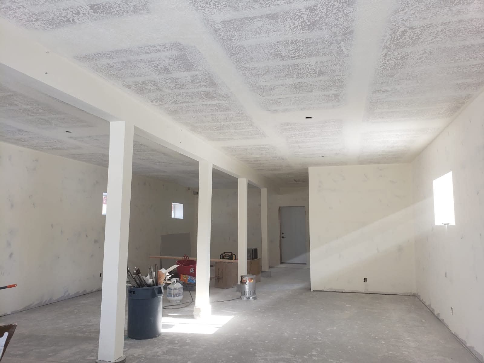 Unfinished interior space with white support columns, textured ceiling, and bare concrete floors.