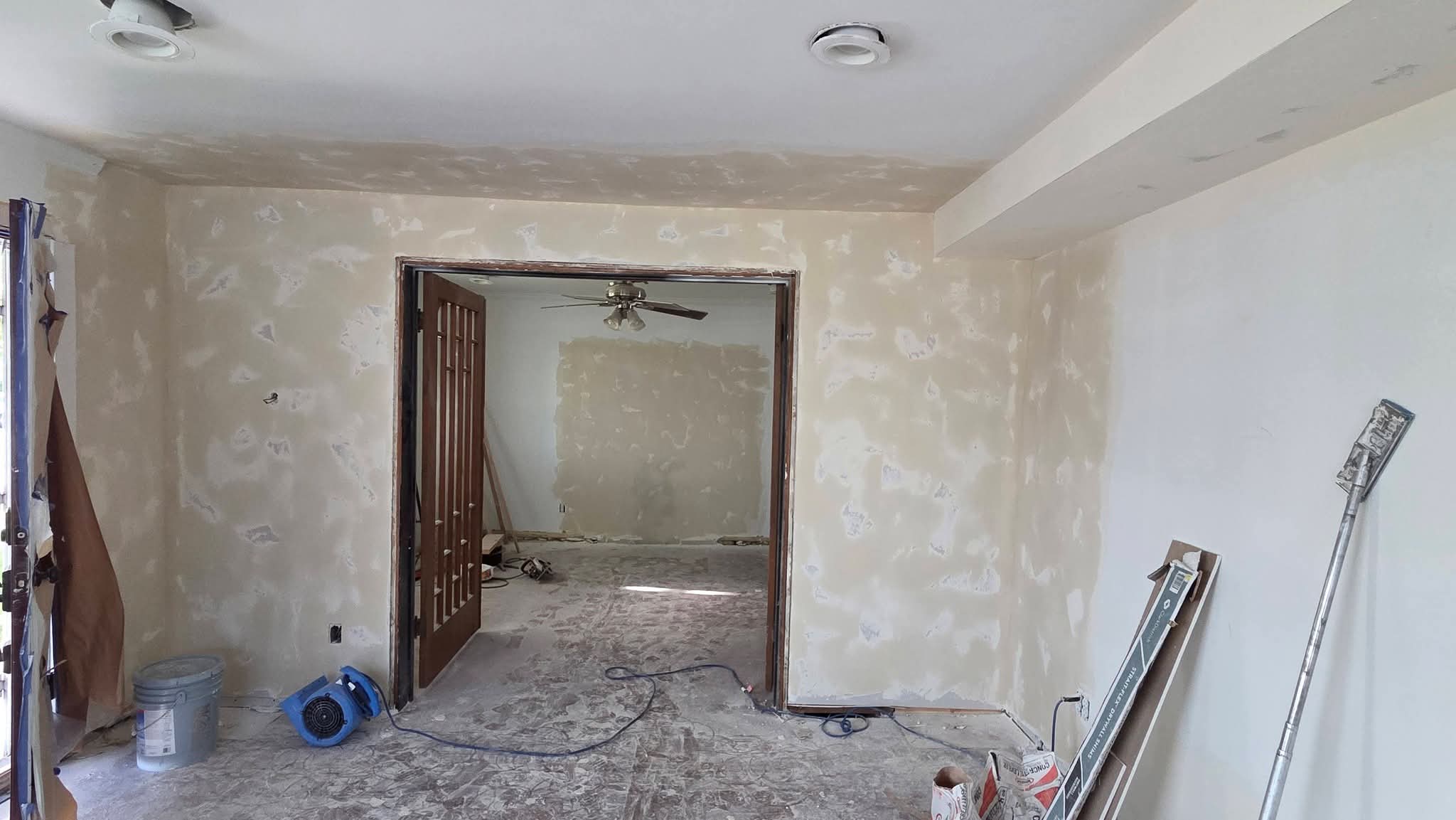 Interior room under renovation with patched drywall, construction tools, and an open wooden doorway.