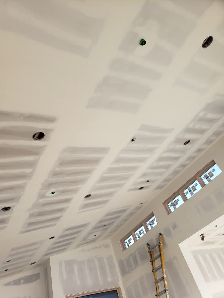 Vaulted ceiling with unfinished drywall, visible joint compound patches, and circular recessed lighting cutouts.
